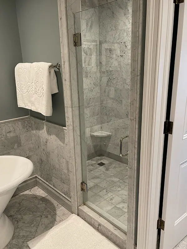 A large glass-enclosed shower featuring floor-to-ceiling light gray marble-patterned tile.