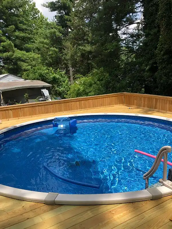 A close-up view of the wooden deck built flush against the blue vinyl liner of the above-ground pool, showing the pool's metal entry ladder.