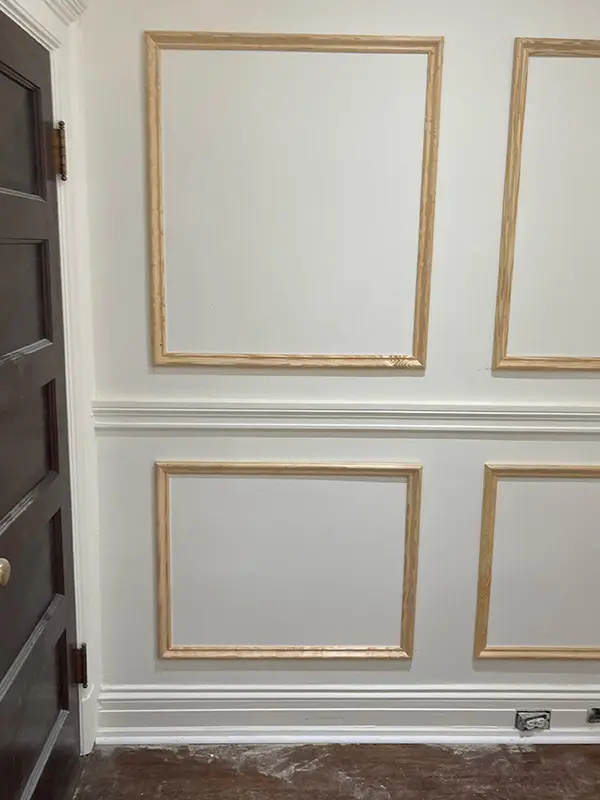 A close-up view of decorative wall paneling where the white picture frame molding is accented with a metallic gold painted inner trim.
